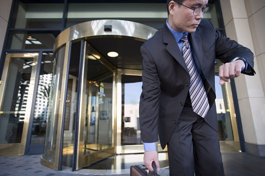 Businessman standing in front of revolving door, checking time on wristwatch, picking up briefcase