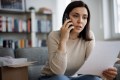 A woman holding a mobile phone to one ear and a piece of paper in her other hand, as if making a complaint to the NSW Ombudsman